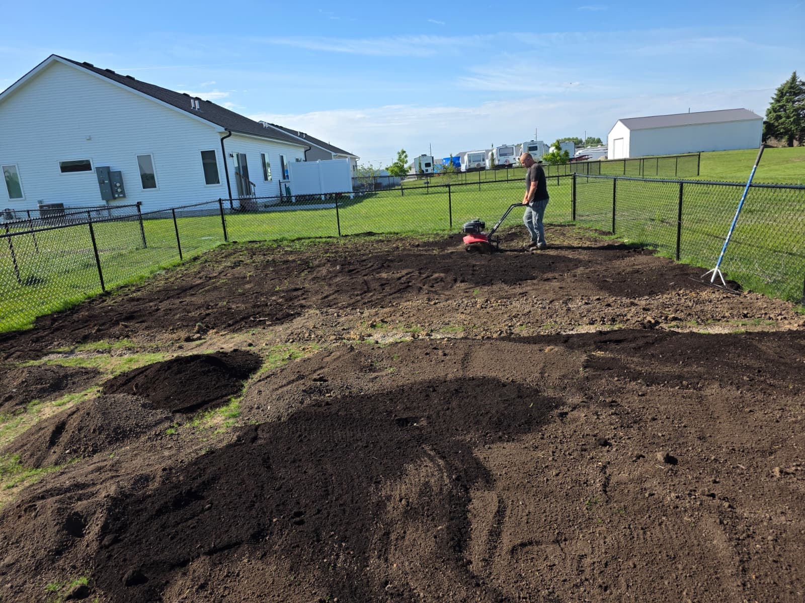 Person using a walk-behind machine across exposed soil inside a fenced yard