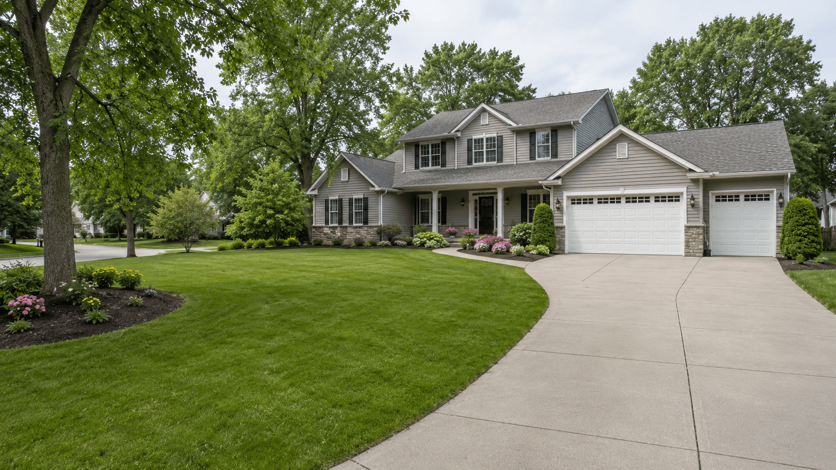 A Des Moines residential property in summer: mowed front lawn, flower beds along the house, mature trees and a concrete driveway